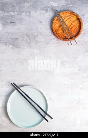Rustic tableware, wooden bowls and ceramic plates with a copy space and chopsticks on stone background Stock Photo