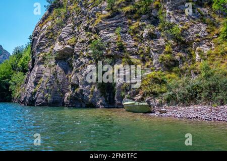 Summer landscape -Albanian rocky mountains, covered with lush foliage and lake with calm blue water, fisher boat on the shore Stock Photo