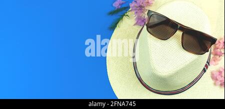 Summer vacation accessories flat lay composition with straw hat and sunglasses on a blue background, top view with copy space Stock Photo