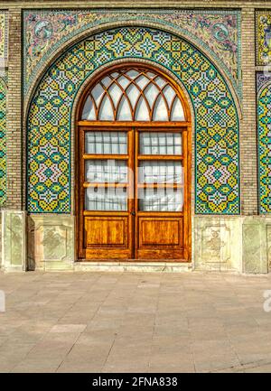 An arched niche, lined with patterns of ceramic tiles, above a two-leaf glazed  wooden door in the territory of the Golestan Palace in Tehran. Stock Photo