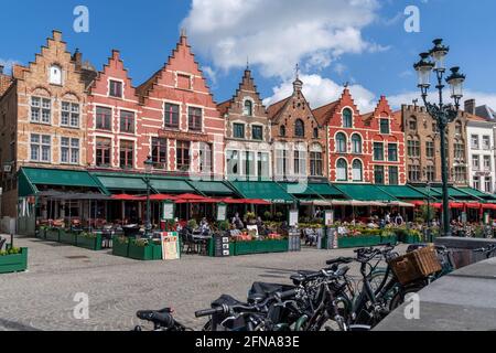 Bruges, Belgium - 12 May, 2021: people enjoy a day out in the restaurants on Market Square in Bruges with many historic brick buildings in the backgro