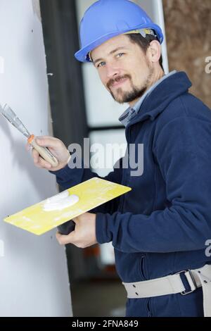 handsome builder in blue working uniform plastering the wall Stock Photo