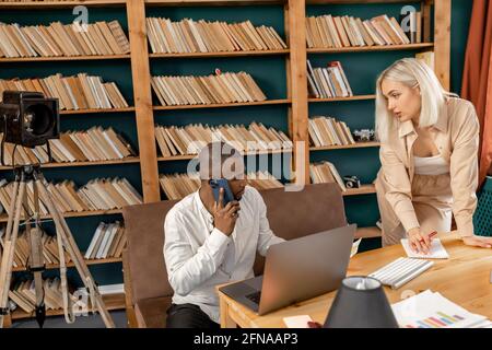 Concentrated partners sit at desk brainstorm working on laptop together, focused multiracial coworkers talk discuss business ideas cooperate using Stock Photo