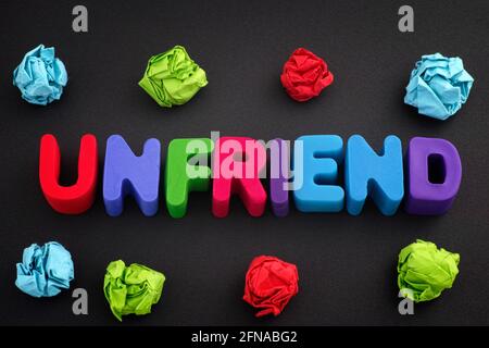 The word Unfriend made out of polymer clay letters with some colorful crumpled paper balls around it. Close up. Stock Photo