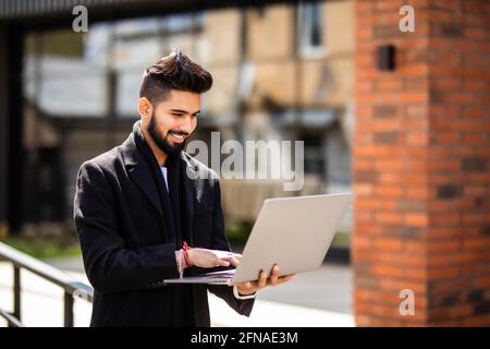 Work in full swing. Young man standing in the street holding a laptop Stock Photo