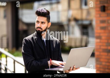 Work in full swing. Young man standing in the street holding a laptop Stock Photo