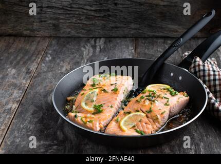 Grilled  salmon fillets with lemon and herbs in roasted pan on wooden table Stock Photo