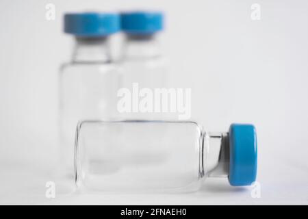 Three glass corona vaccine bottles with blue cap on a white background. Two standing and one lying. Shallow depth of field. Copy space Stock Photo