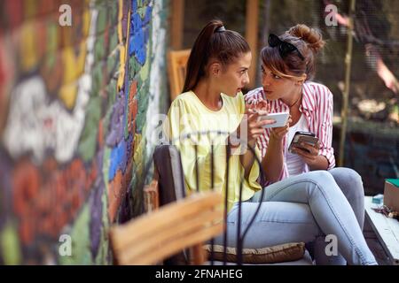 Two female friends gossip while sitting in a relaxed atmosphere in the bar. Leisure, bar, friendship, outdoor Stock Photo