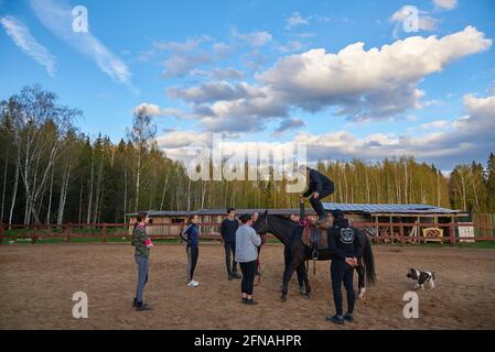 Russia, Moscow region, May 2021. A teenage girl is studying horse riding at an equestrian school. A girl stands on the back of a horse.