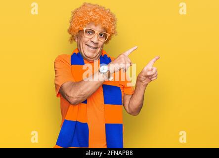 Senior hispanic man football hooligan cheering game smiling and looking at the camera pointing with two hands and fingers to the side. Stock Photo