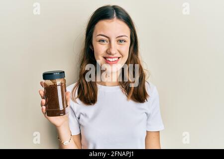 Young brunette woman holding soluble coffee looking positive and happy standing and smiling with a confident smile showing teeth Stock Photo