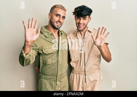 Homosexual gay couple standing together wearing casual jumpsuit waiving saying hello happy and smiling, friendly welcome gesture Stock Photo