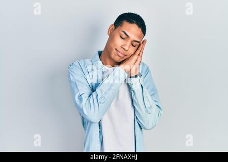 Young african american guy wearing casual clothes sleeping tired dreaming and posing with hands together while smiling with closed eyes. Stock Photo