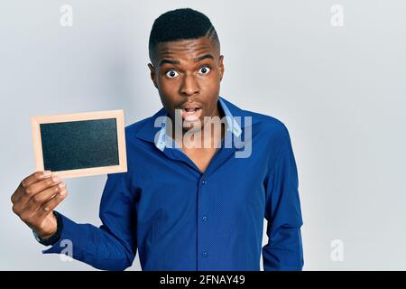 Young african american man holding empty frame scared and amazed with open mouth for surprise, disbelief face Stock Photo