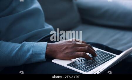 Closeup view of hands of a guy using a laptop placed on his lap and holding phone . High quality photo Stock Photo