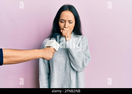 Young hispanic girl being interviewed by reporter holding microphone feeling unwell and coughing as symptom for cold or bronchitis. health care concep Stock Photo