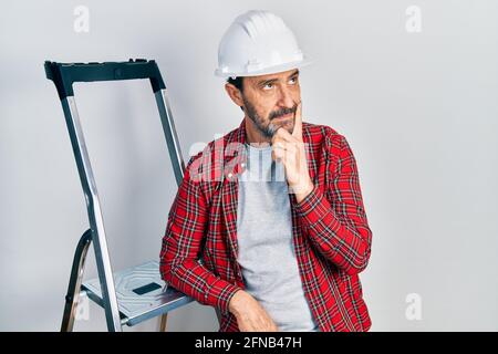 Middle age hispanic worker man using ladder serious face thinking about question with hand on chin, thoughtful about confusing idea Stock Photo