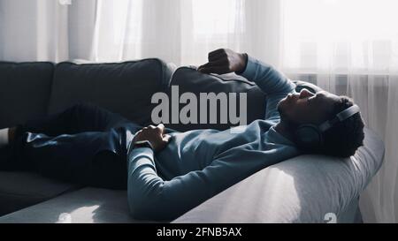 African American man wearing headphones listening to music. Lying on The Couch. High quality photo Stock Photo