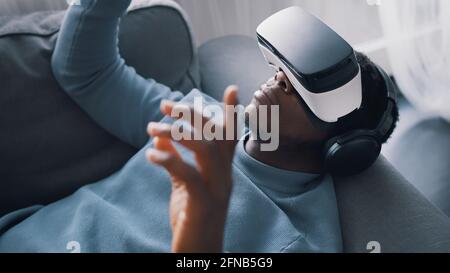 African-American man wearing virtual reality glasses and headset lying on the sofa. High quality photo Stock Photo
