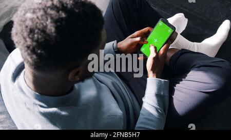 Man Sitting Cross-Legged On The Couch Using A cell phone with a green screen. High quality photo Stock Photo