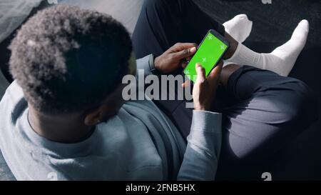 Man Sitting Cross-Legged On The Couch Using A cell phone with a green screen. High quality photo Stock Photo