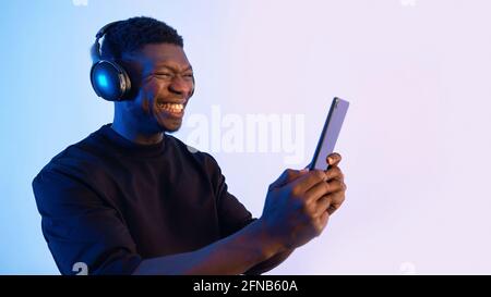 Guy wearing headphones and holding a tablet watching some video. Intense expressions on his face. Blue background. Closeup of a guy using a tablet watching media. . High quality photo Stock Photo