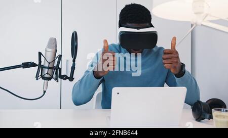Black man wearing a virtual reality glasses sitting at the table in front of his laptop. Man watching something in the 360 degree virtual environment using the VR glasses. Relaxing. High quality photo Stock Photo