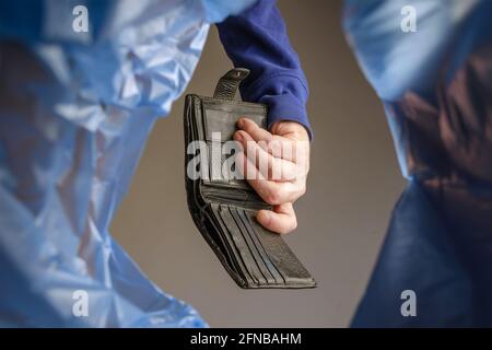 A hand tosses an old black wallet into a trash can. Man holds empty leather purse over garbage basket. View from below. Indoors. Stock Photo