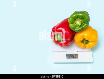 The concept of diet, proper nutrition, healthy eating. Three multicolored fresh yellow red green bell peppers with water droplets on kitchen scales is Stock Photo