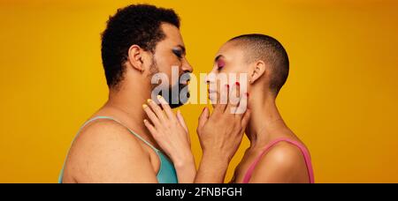 Affectionate gender fluid couple. Non binary male and female touching each other face with their eyes closed on yellow background. Stock Photo