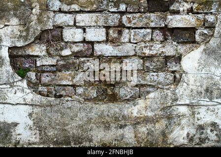 A heavily weathered and textured brick wall beneath broken plaster Stock Photo