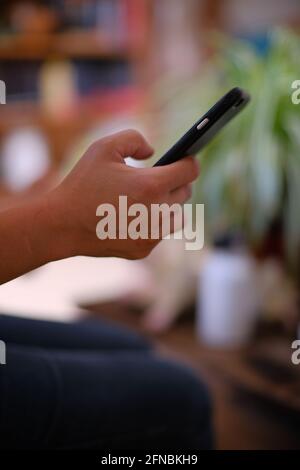 Asian Filipino girl or woman holding a cell phone and typing with her thumb in Cournonsec near Montpellier, Occitanie, South of France Stock Photo