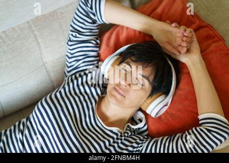Middle-aged woman listening to soothing music with headphones lying on her sofa. Stock Photo
