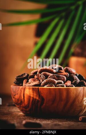 Unpeeled organic cocoa bean in bowl on wooden rustic table background. Copy space Stock Photo