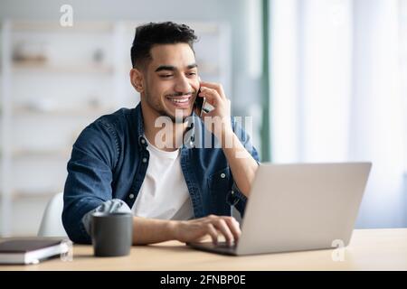 Successful middle-eastern guy talking on phone while working at home Stock Photo