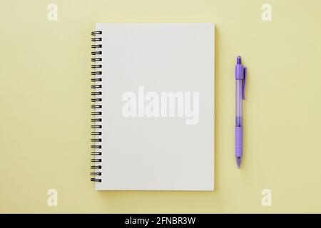 Spiral Notebook or Spring Notebook in Unlined Type and Purple Pen on Pastel Yellow Minimalist Background. Spiral Notebook Mock up on Center Frame Stock Photo