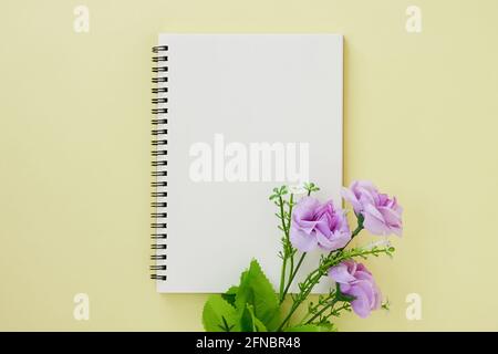 Spiral Notebook or Spring Notebook in Unlined Type and Purple Flower on Pastel Yellow Minimalist Background. Spiral Notebook Mock up on Center Frame Stock Photo