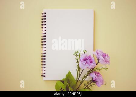Spiral Notebook or Spring Notebook in Unlined Type and Purple Flower on Pastel Yellow Minimalist Background. Spiral Notebook Mock up on Center Frame i Stock Photo