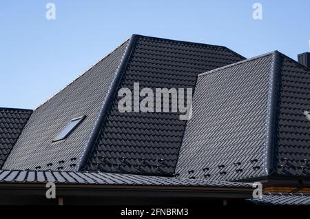 Brown corrugated metal profile roof installed on a modern house with a attic windows. The roof of corrugated sheet. Roofing of metal profile wavy Stock Photo