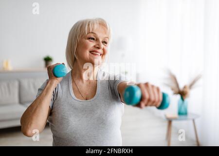 Mature woman exercising at home with two dumbbells Stock Photo