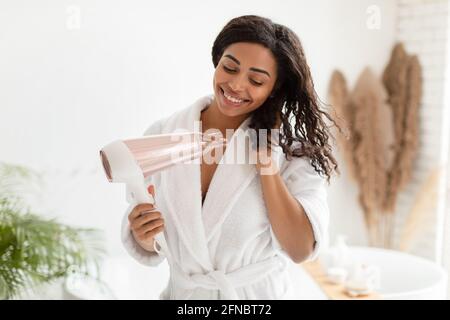 Happy Black Lady Drying Wavy Hair With Hairdryer In Bathroom Stock Photo