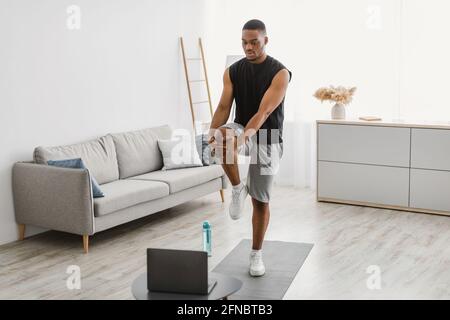 African Man Doing Standing Knee To Chest Exercise At Home Stock Photo