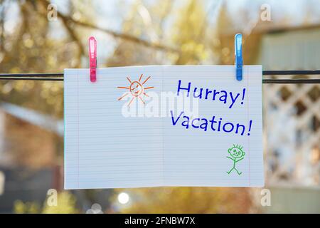 School notebook with the inscription - Hooray, Vacation, hanging on clothespins. Stock Photo
