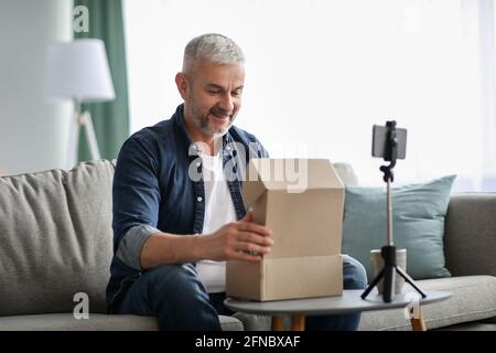 Happy senior man blogger broadcasting while opening delivery box Stock Photo