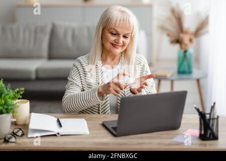 Smiling mature woman spraying sanitizer on hand Stock Photo