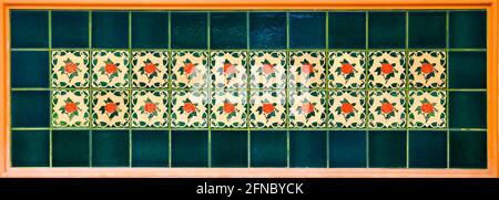 Colourful ceramic tile mosaic with red rose tiles with a  bottle green border. Typical of the designs found on the facades of traditional Chinese shop Stock Photo