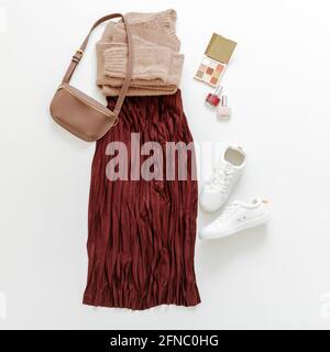 Folded clothes for women fashion urban basic outfit. Female spring look autumn outfit burgundy skirt beige sweater white shoes sneakers bag, make up Stock Photo