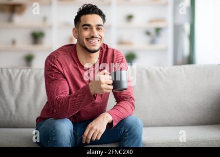 Cheerful arab guy sitting on couch and drinking tea Stock Photo