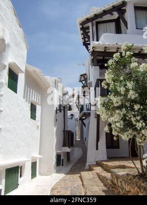 Typical Spanish construction of a narrow alley between white beach houses built according to Cycladic architecture in Menorca. Stock Photo